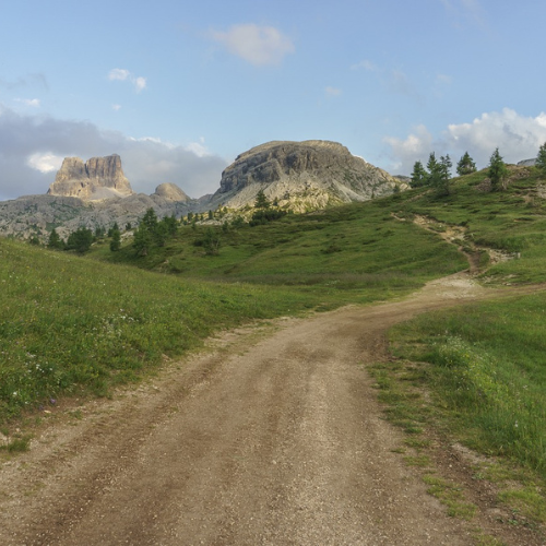 A dirt road winding into the distance with a mountain in the background on a sunny day.